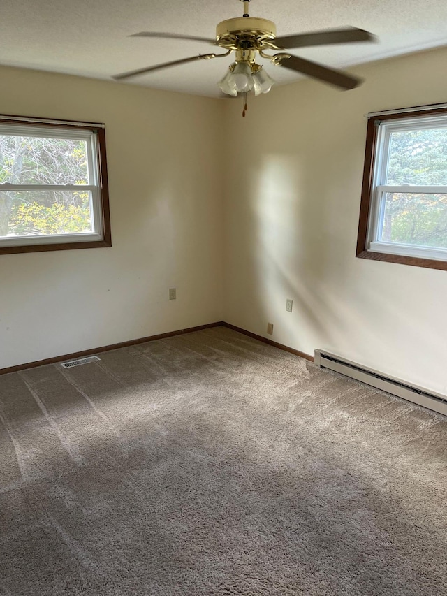 carpeted empty room with ceiling fan, a baseboard radiator, and a healthy amount of sunlight