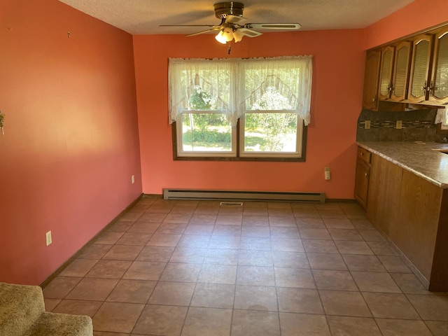 interior space with a baseboard heating unit, ceiling fan, light tile patterned flooring, and a textured ceiling