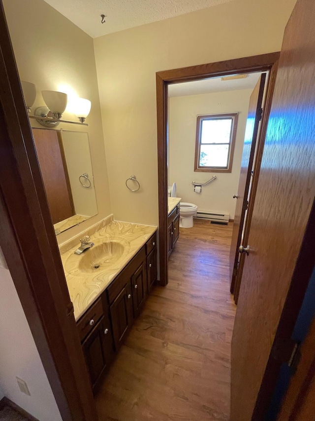 bathroom with vanity, a textured ceiling, baseboard heating, hardwood / wood-style flooring, and toilet