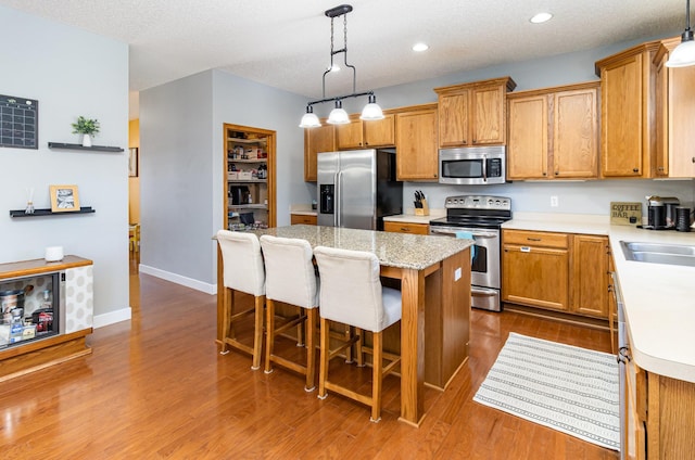 kitchen with appliances with stainless steel finishes, light countertops, decorative light fixtures, and a center island