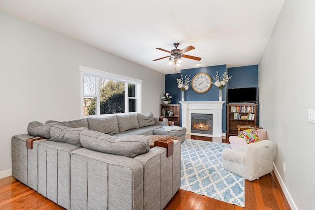 living room with a fireplace with flush hearth, wood finished floors, baseboards, and ceiling fan