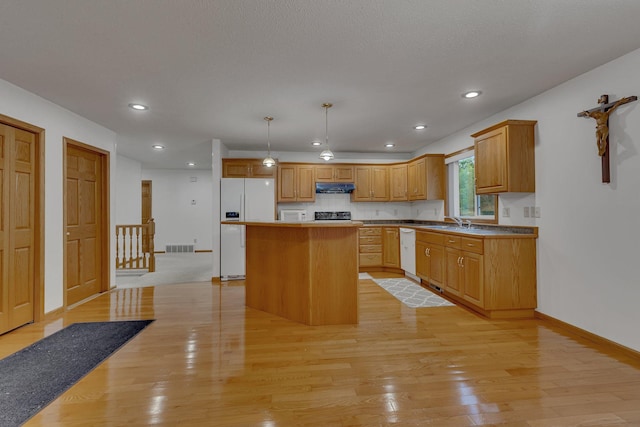 kitchen with pendant lighting, white appliances, a center island, and light hardwood / wood-style flooring