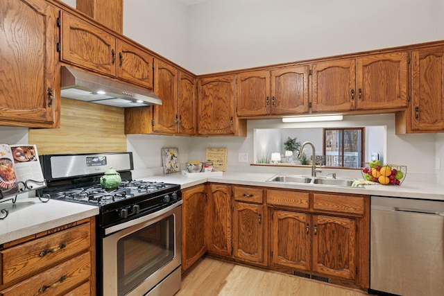 kitchen featuring brown cabinetry, a sink, under cabinet range hood, and stainless steel appliances