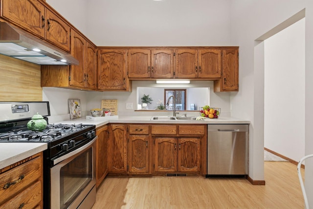 kitchen featuring brown cabinets, under cabinet range hood, a sink, light wood-type flooring, and appliances with stainless steel finishes