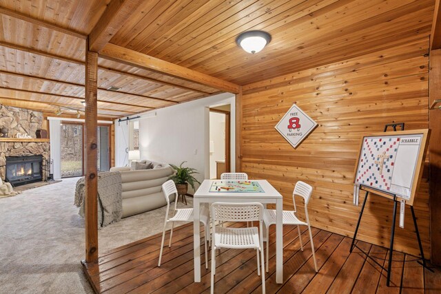 dining area with wooden walls, a fireplace, wooden ceiling, wood-type flooring, and beam ceiling