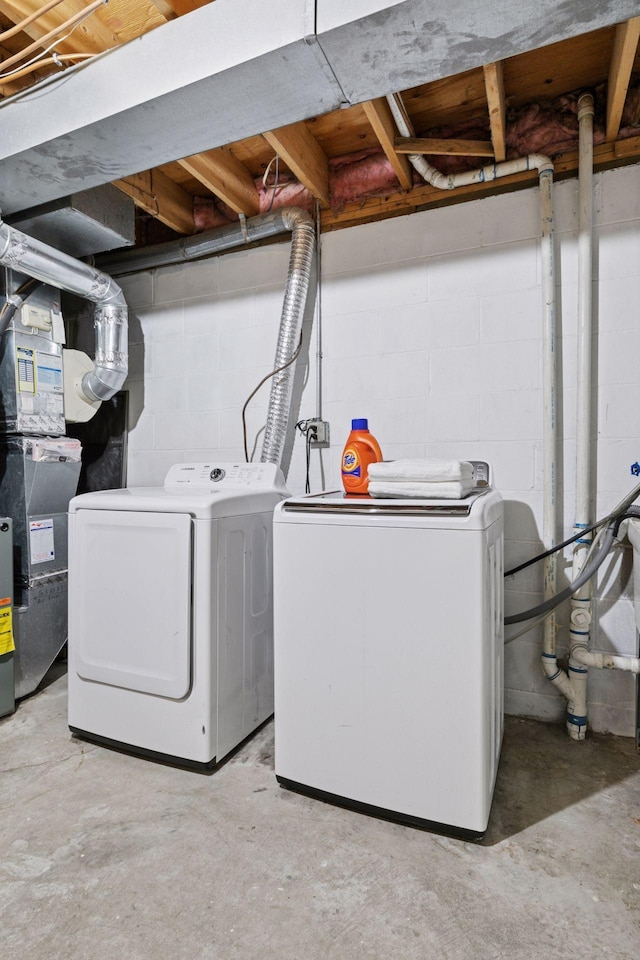 clothes washing area with concrete block wall, separate washer and dryer, heating unit, and laundry area