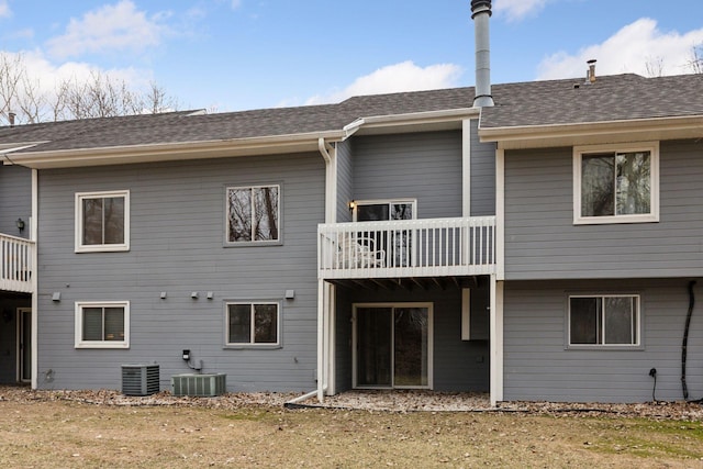 rear view of house featuring cooling unit, roof with shingles, and a balcony