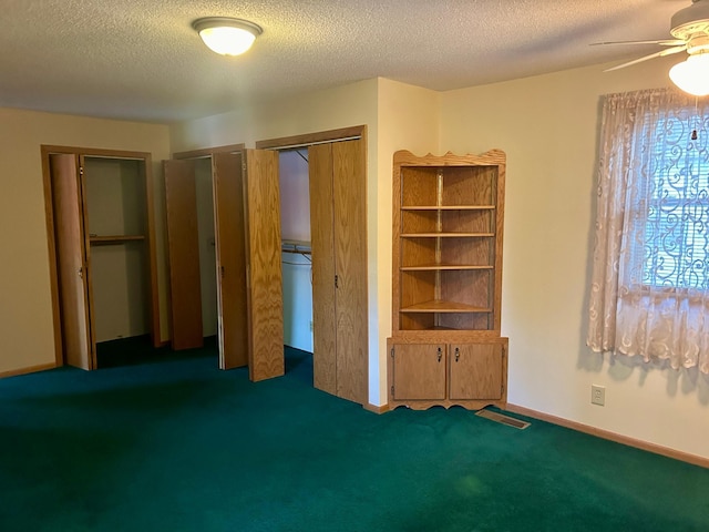 unfurnished bedroom featuring a textured ceiling, dark carpet, ceiling fan, and multiple closets