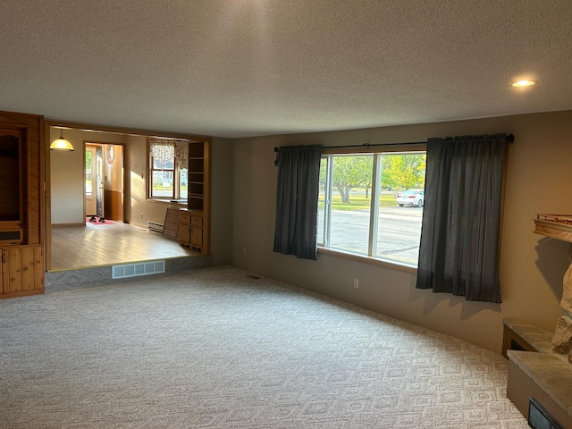 unfurnished living room featuring light carpet, a textured ceiling, baseboard heating, and a tiled fireplace