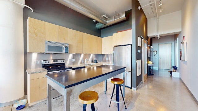 kitchen featuring appliances with stainless steel finishes, light brown cabinets, a high ceiling, and backsplash