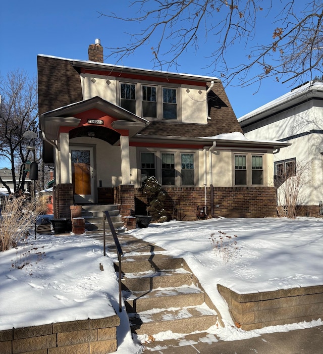 view of front of property featuring stucco siding, a shingled roof, a chimney, and brick siding