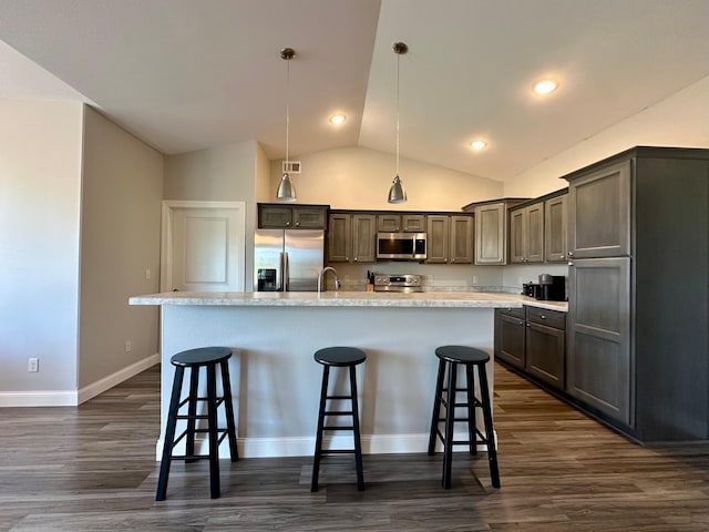 kitchen with an island with sink, stainless steel appliances, hanging light fixtures, and a kitchen breakfast bar