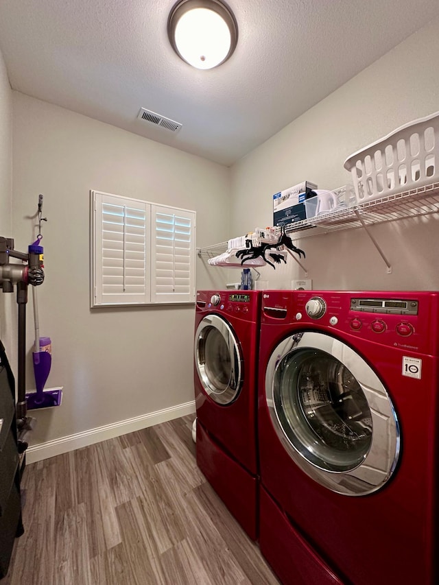 clothes washing area featuring washing machine and clothes dryer, wood-type flooring, and a textured ceiling