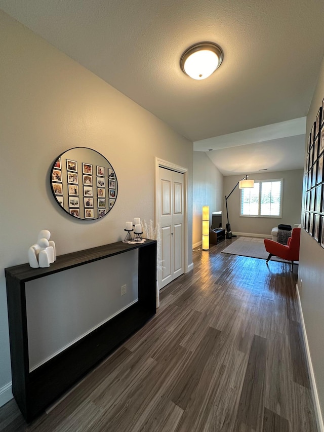 hallway featuring a textured ceiling, vaulted ceiling, and dark wood-type flooring