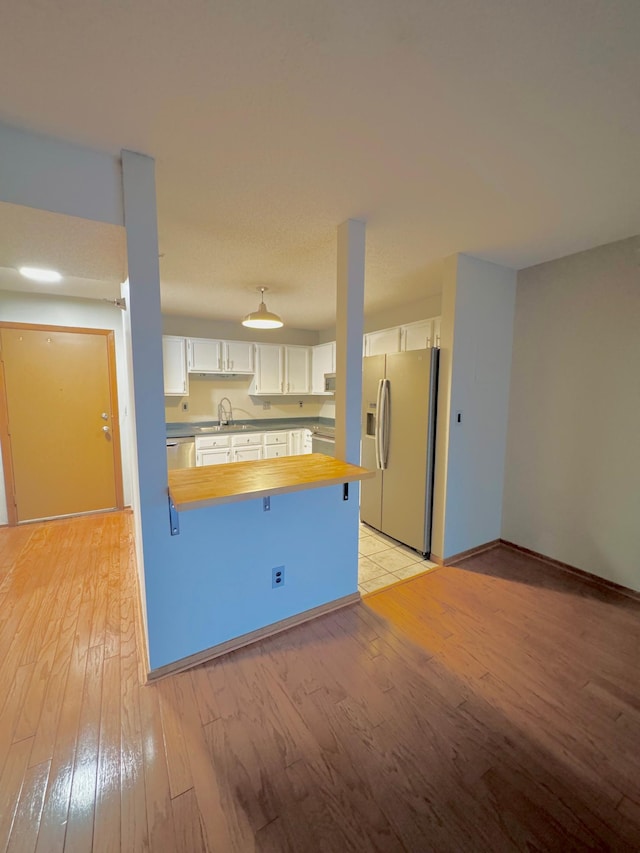 kitchen featuring light wood-style floors, white cabinetry, fridge with ice dispenser, a sink, and butcher block countertops