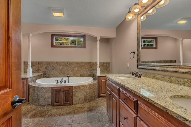 bathroom with decorative columns, vanity, and tiled bath