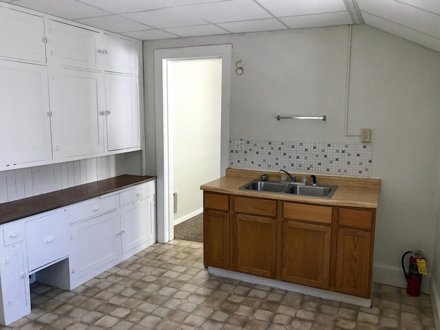 kitchen with sink, white cabinets, vaulted ceiling, decorative backsplash, and a drop ceiling