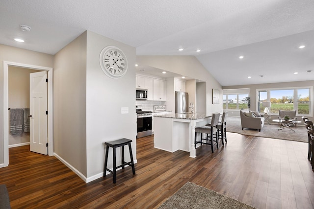 kitchen featuring a breakfast bar, dark hardwood / wood-style floors, a kitchen island with sink, white cabinetry, and appliances with stainless steel finishes