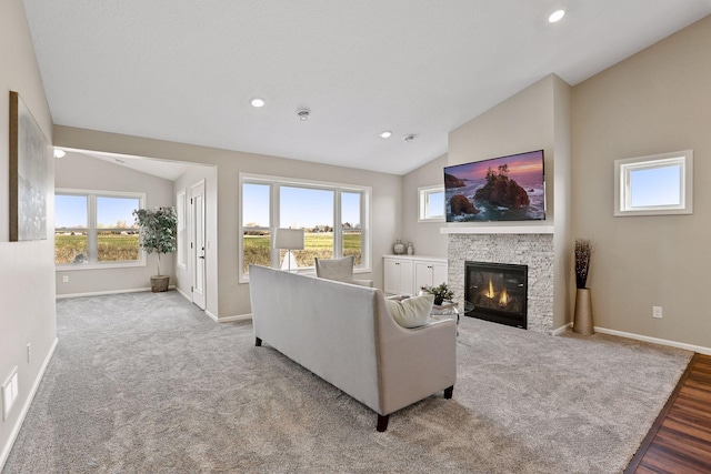 living room with light wood-type flooring, a stone fireplace, vaulted ceiling, and a wealth of natural light