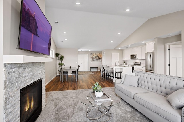 living room with a stone fireplace, vaulted ceiling, dark hardwood / wood-style flooring, and sink