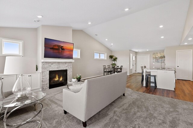 living room featuring a stone fireplace, lofted ceiling, dark hardwood / wood-style flooring, and a wealth of natural light