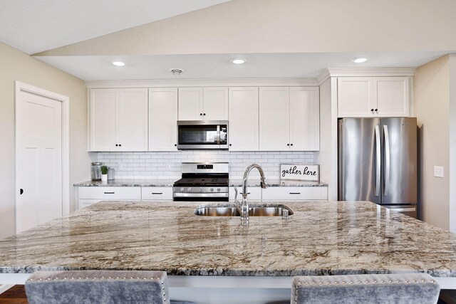 kitchen with stainless steel appliances, vaulted ceiling, white cabinetry, and a kitchen island with sink