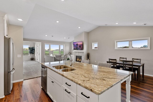 kitchen with a kitchen island with sink, vaulted ceiling, white cabinetry, a kitchen bar, and appliances with stainless steel finishes