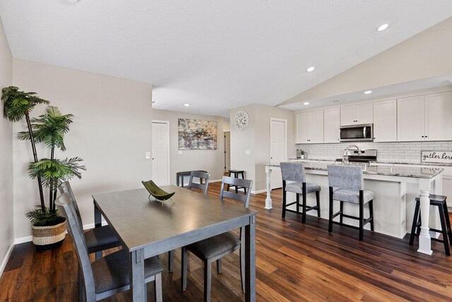 dining area featuring vaulted ceiling, sink, and dark wood-type flooring