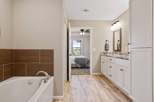 bathroom featuring a textured ceiling, a tub to relax in, hardwood / wood-style floors, ceiling fan, and vanity