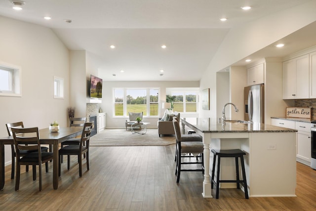 kitchen with sink, a breakfast bar area, lofted ceiling, stainless steel refrigerator with ice dispenser, and a center island with sink