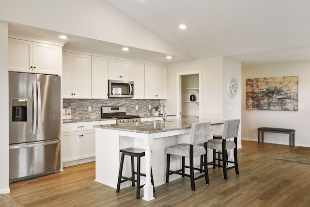 kitchen featuring an island with sink, lofted ceiling, sink, white cabinetry, and appliances with stainless steel finishes