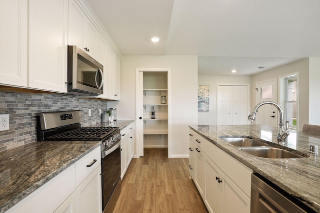 kitchen featuring dark stone countertops, white cabinets, stainless steel appliances, and sink