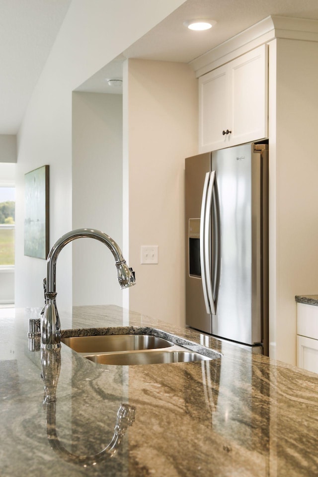 kitchen featuring dark stone countertops, white cabinetry, sink, and stainless steel fridge