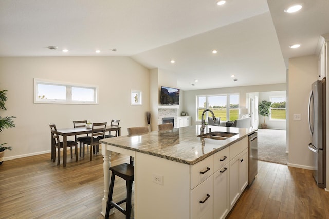 kitchen featuring an island with sink, lofted ceiling, sink, stone counters, and stainless steel appliances