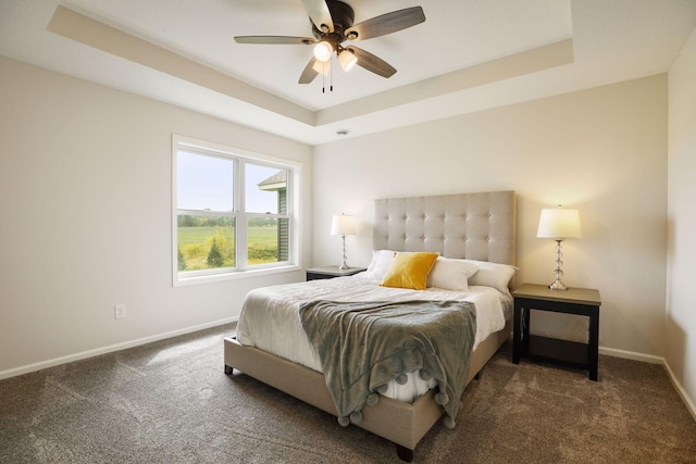 bedroom featuring ceiling fan, a raised ceiling, and dark carpet