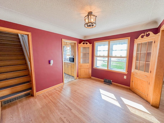 empty room with an inviting chandelier, light hardwood / wood-style floors, and a textured ceiling