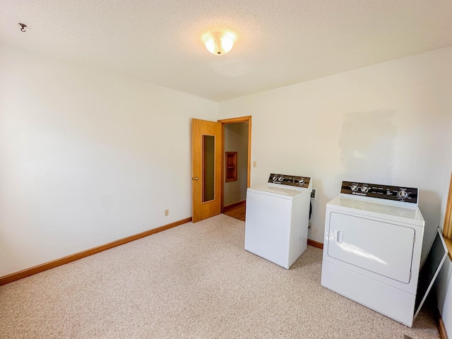 clothes washing area featuring a textured ceiling, light colored carpet, and washing machine and dryer