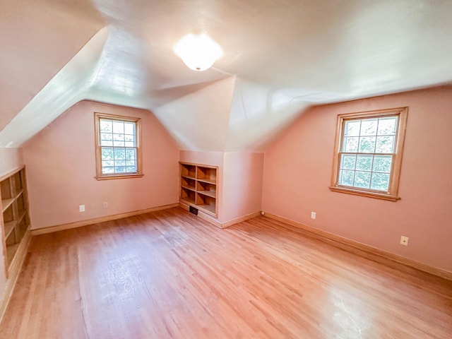 additional living space with built in shelves, lofted ceiling, and light hardwood / wood-style floors