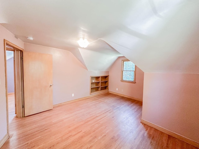 additional living space featuring light wood-type flooring, lofted ceiling, and built in features