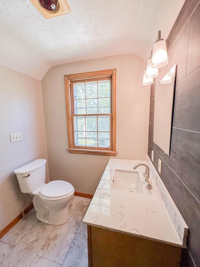 bathroom with lofted ceiling, a textured ceiling, vanity, and toilet