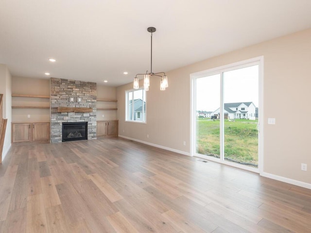 unfurnished living room featuring a stone fireplace, a chandelier, and light wood-type flooring