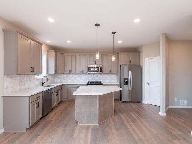 kitchen featuring a kitchen island, appliances with stainless steel finishes, sink, light hardwood / wood-style floors, and decorative light fixtures