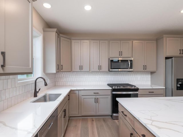 kitchen featuring decorative backsplash, light hardwood / wood-style flooring, sink, appliances with stainless steel finishes, and light stone counters