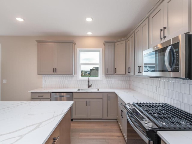 kitchen featuring decorative backsplash, light stone counters, appliances with stainless steel finishes, light hardwood / wood-style flooring, and sink