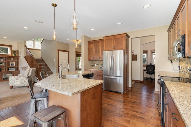 kitchen with light stone countertops, a kitchen island with sink, stainless steel appliances, dark wood-type flooring, and sink