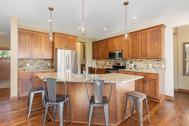 kitchen with an island with sink, sink, decorative light fixtures, dark wood-type flooring, and stainless steel appliances