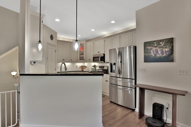 kitchen with hanging light fixtures, kitchen peninsula, backsplash, stainless steel appliances, and light hardwood / wood-style floors