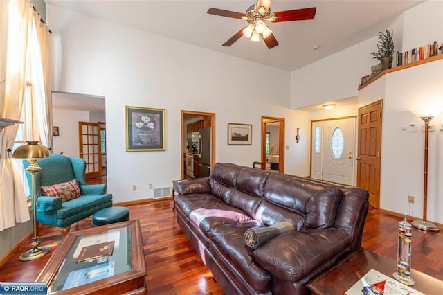 living room with ceiling fan, a towering ceiling, and dark hardwood / wood-style flooring