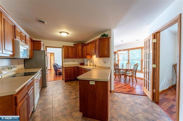 kitchen with hanging light fixtures, sink, kitchen peninsula, white appliances, and dark hardwood / wood-style flooring