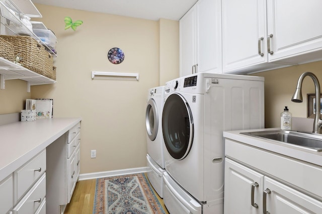 laundry area with sink, washing machine and dryer, light wood-type flooring, and cabinets